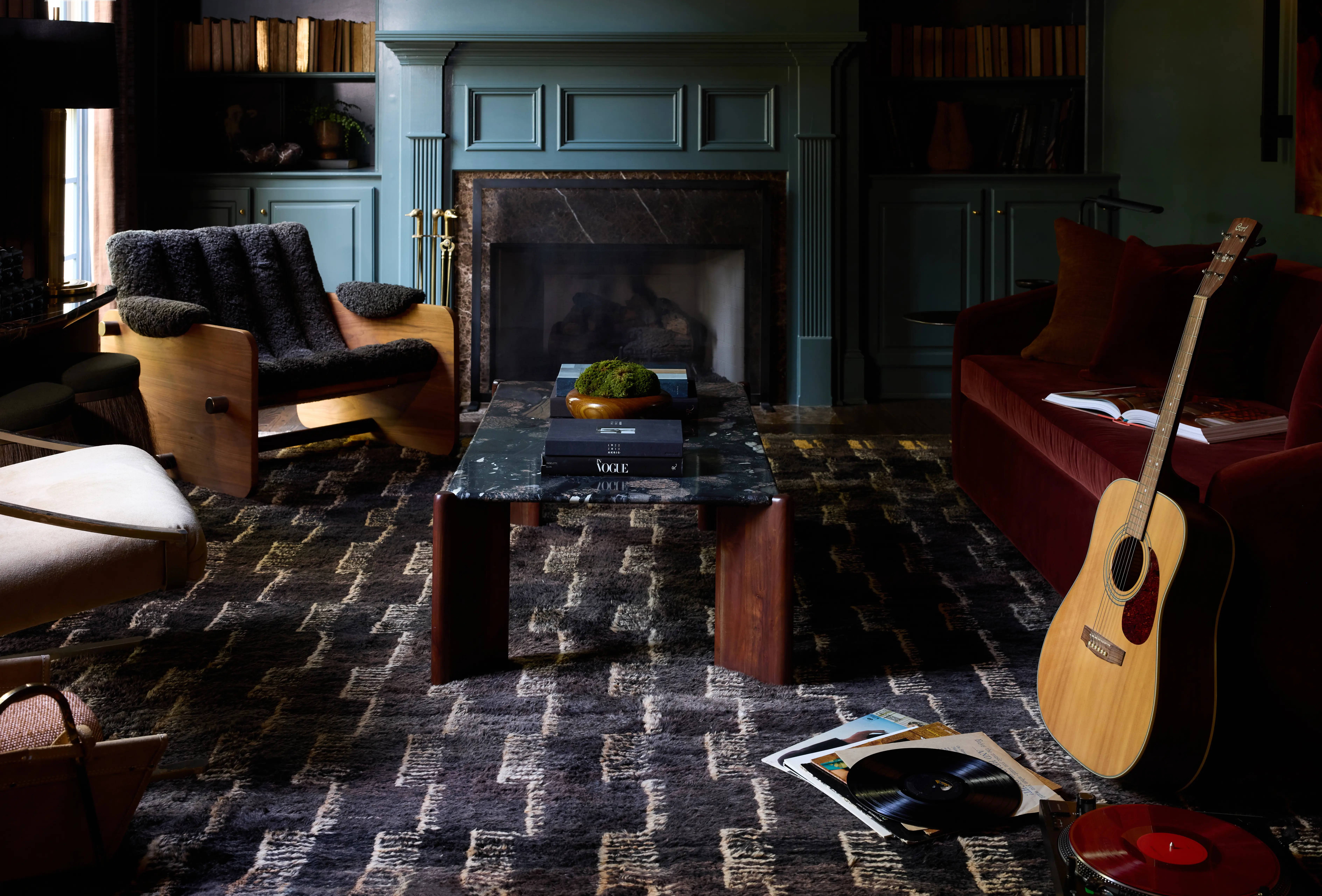 Cozy living room with dark patterned rug, fireplace, wooden chair, red sofa, guitar, and vinyl records.