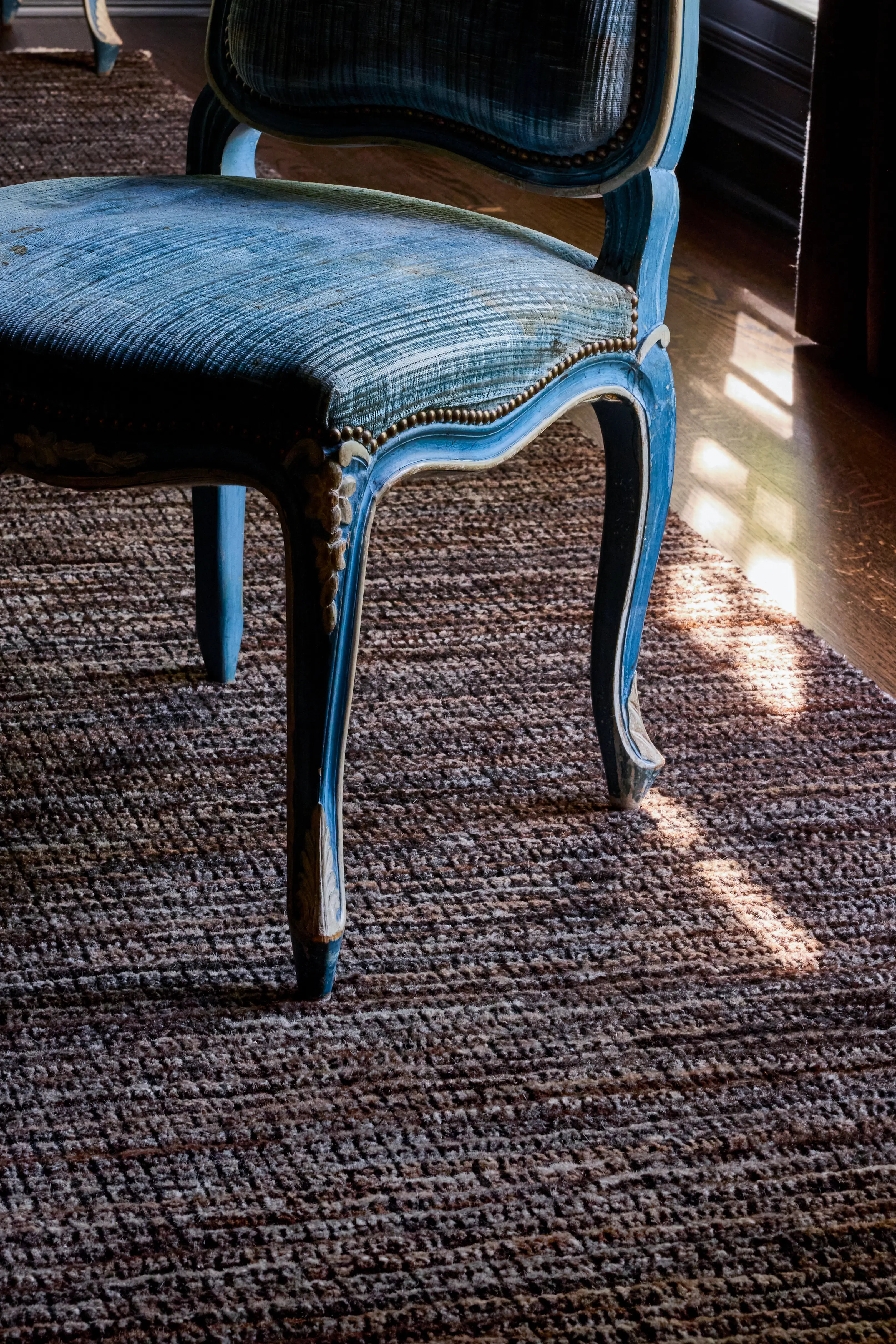 Close-up of a vintage blue upholstered chair with carved wooden legs on a textured brown carpet.