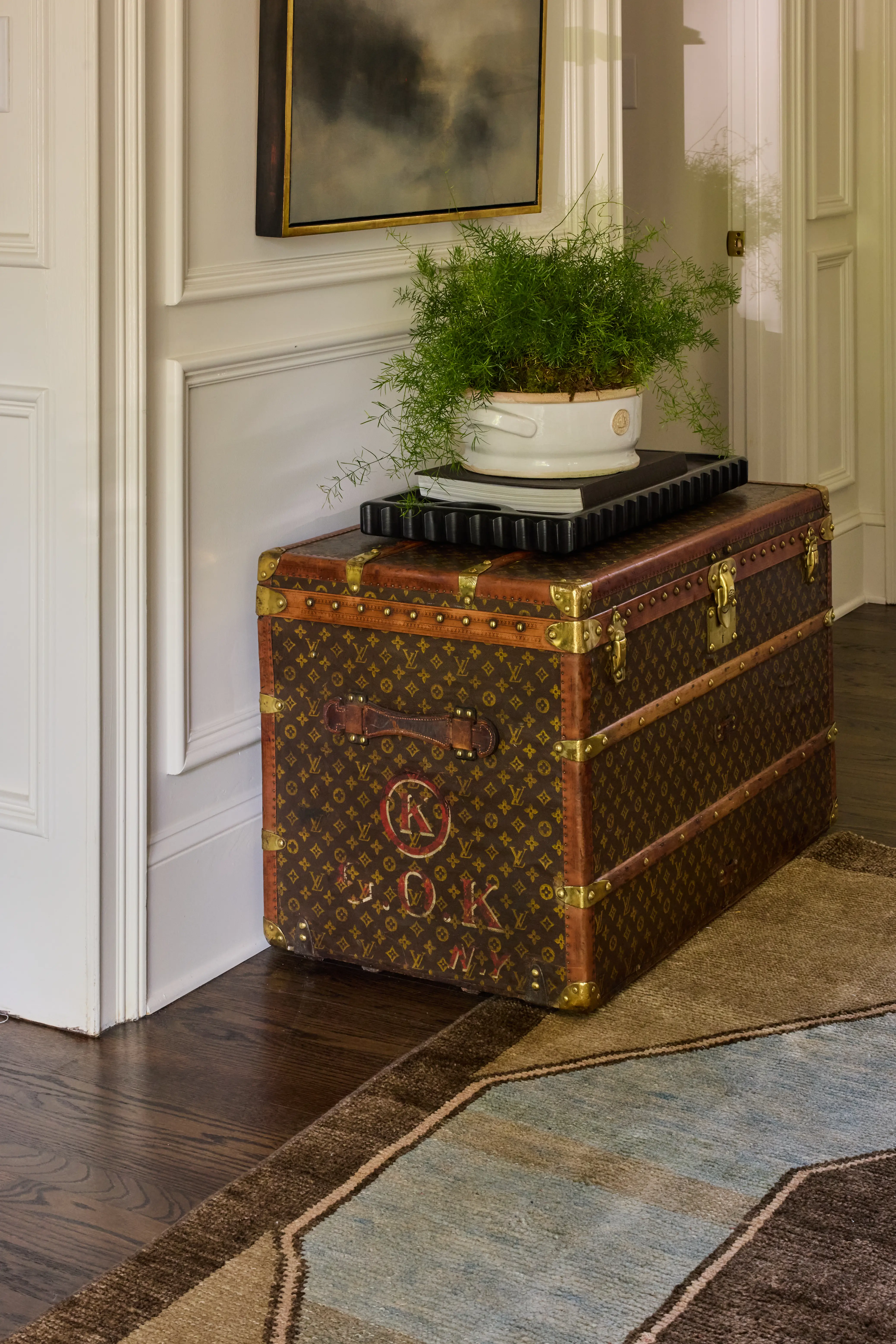 Decorative vintage Louis Vuitton trunk with plant and books on top in a cozy indoor setting.