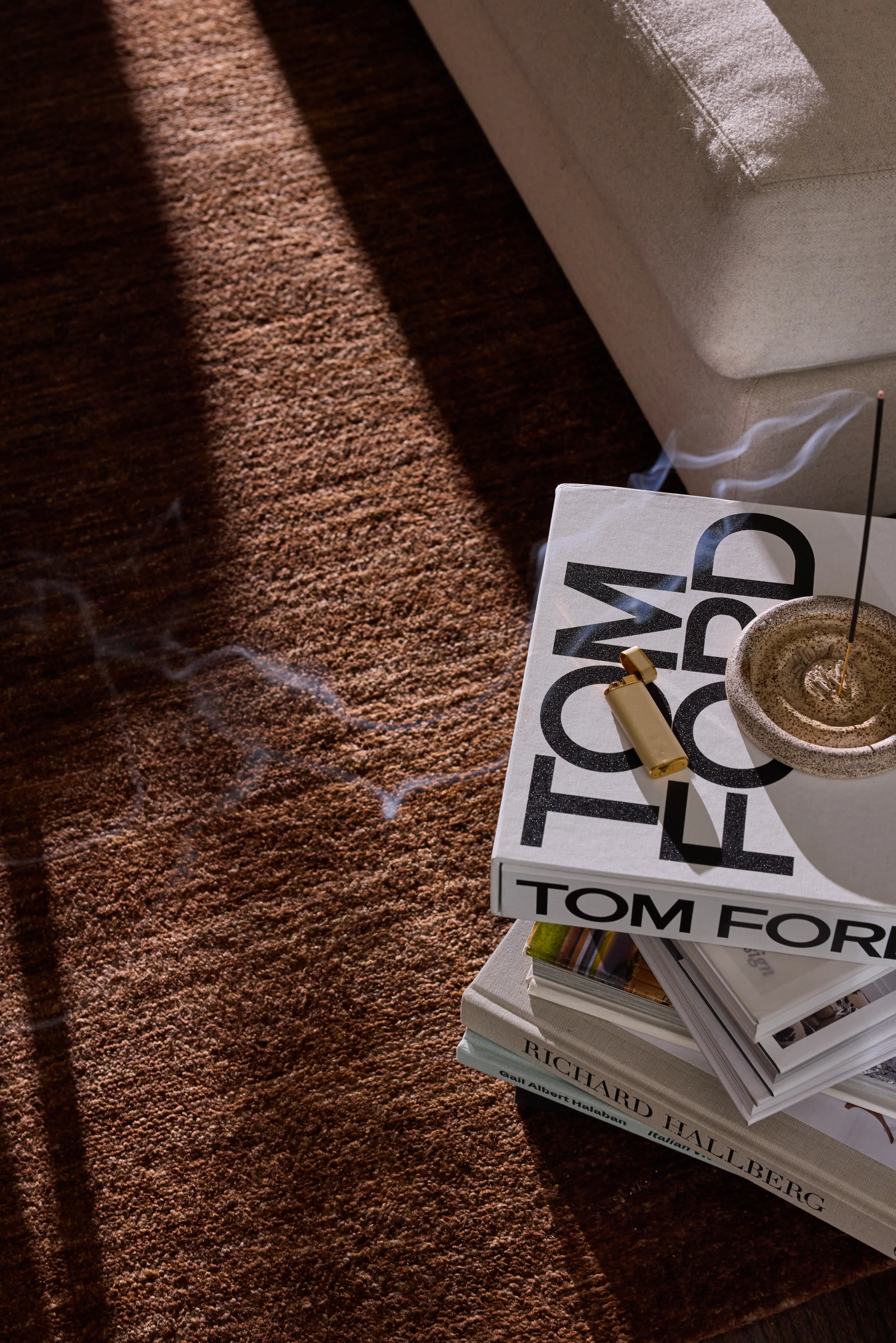 Stack of large books on brown carpet with a lighter and a lit incense stick creating smoke.