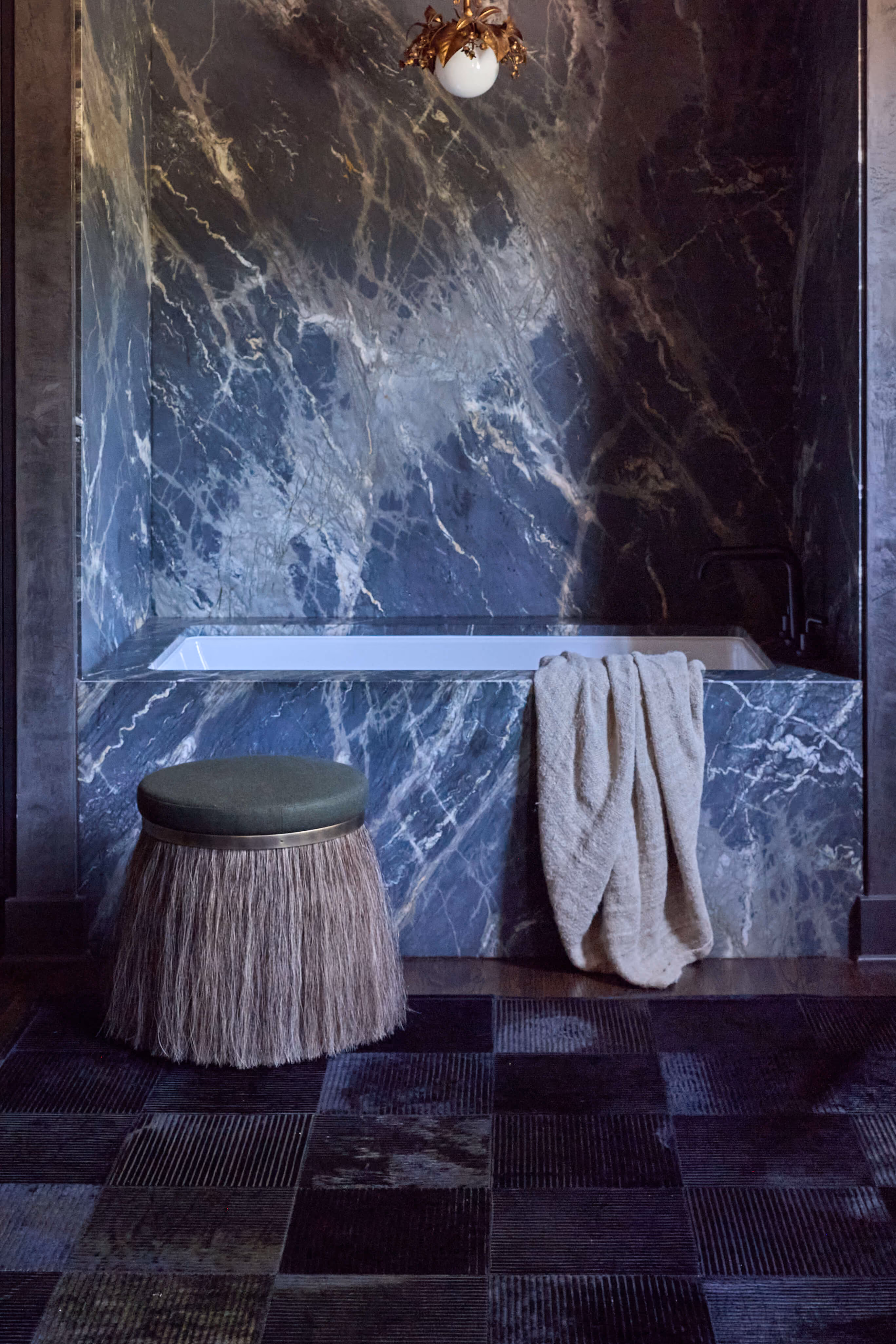 Modern bathroom with a blue marble bathtub, a beige towel, and a fringed stool with a green cushion.