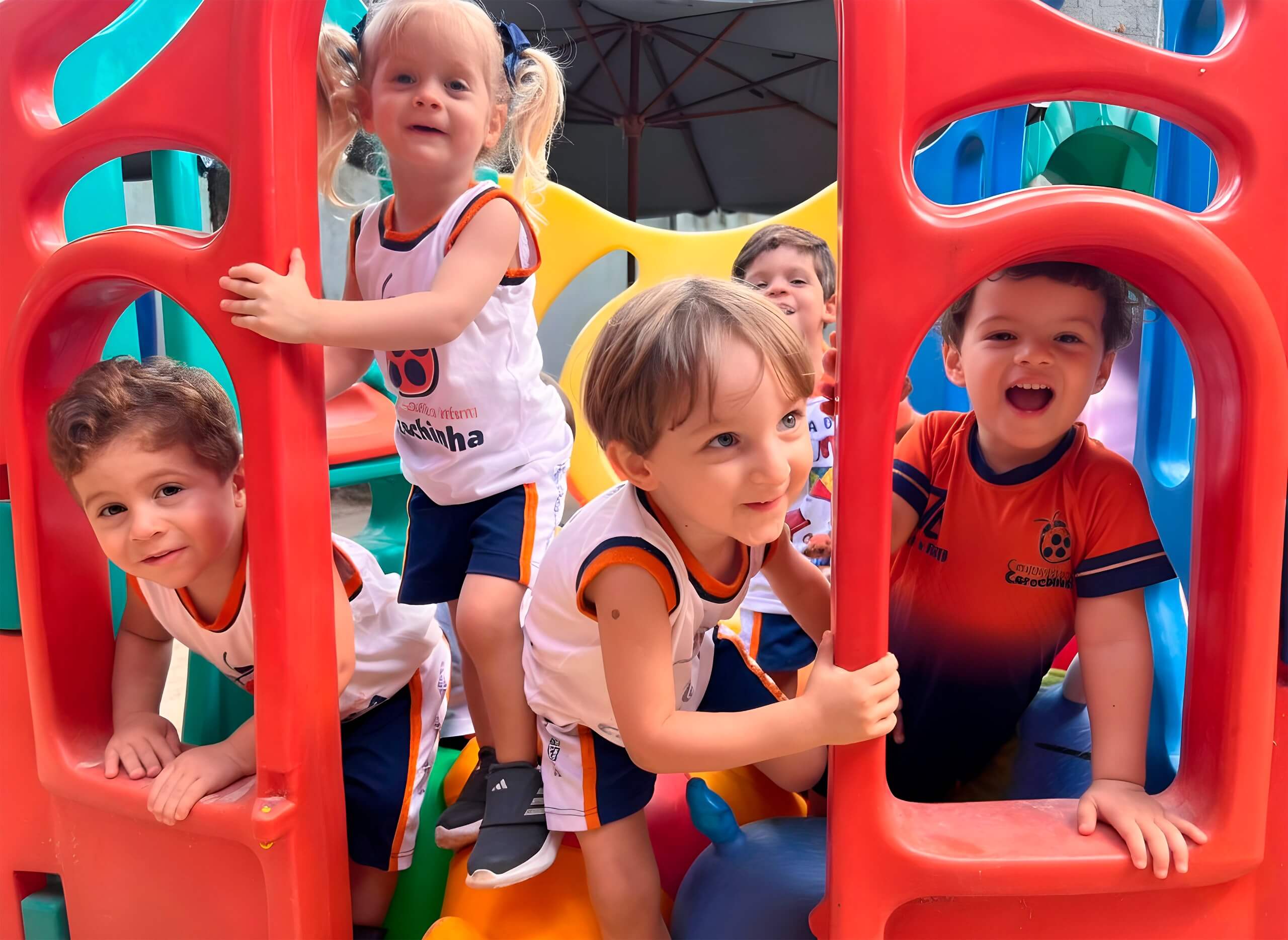Crianças da educação infantil do Centro Escolar Carochinha brincando no parquinho colorido ao ar livre, em contato com a natureza, na escola localizada na Zona Norte do Recife, em um ambiente alegre e seguro.