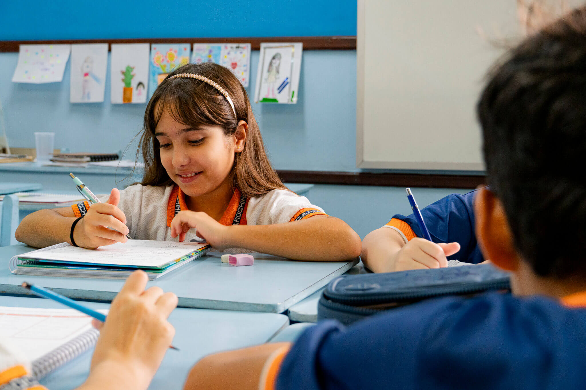 Aluna do ensino fundamental anos iniciais do Centro Escolar Carochinha em Recife, estudando em sala de aula com atividades de escrita e aprendizagem, em ambiente acolhedor e estimulante.
