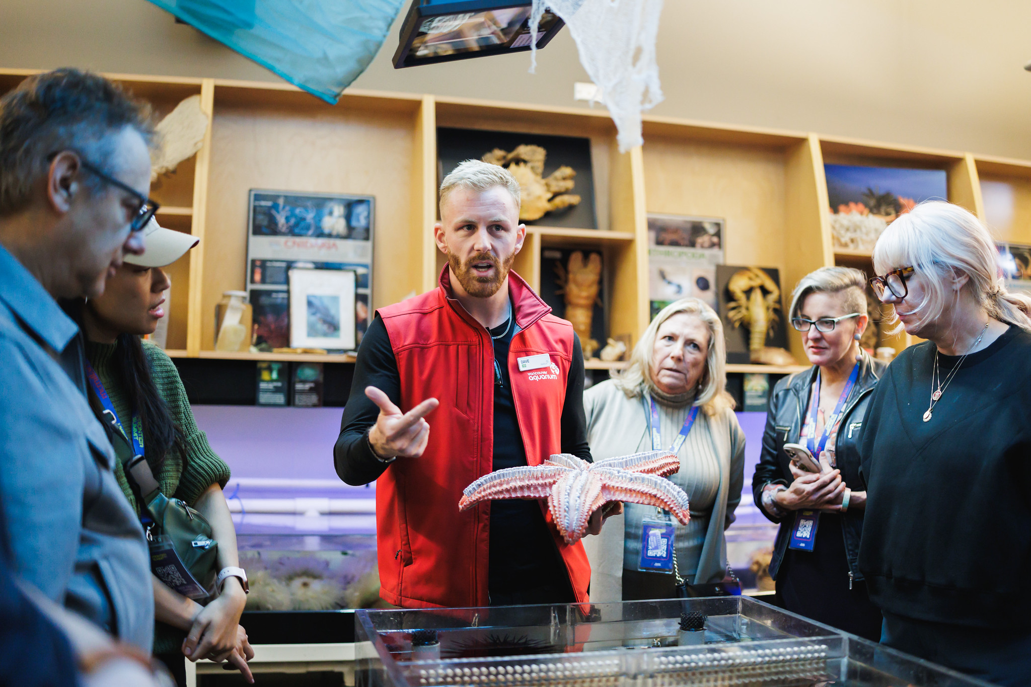 A Vancouver Aquarium staff member holds up a large sea star while attendees gather around a touch tank.