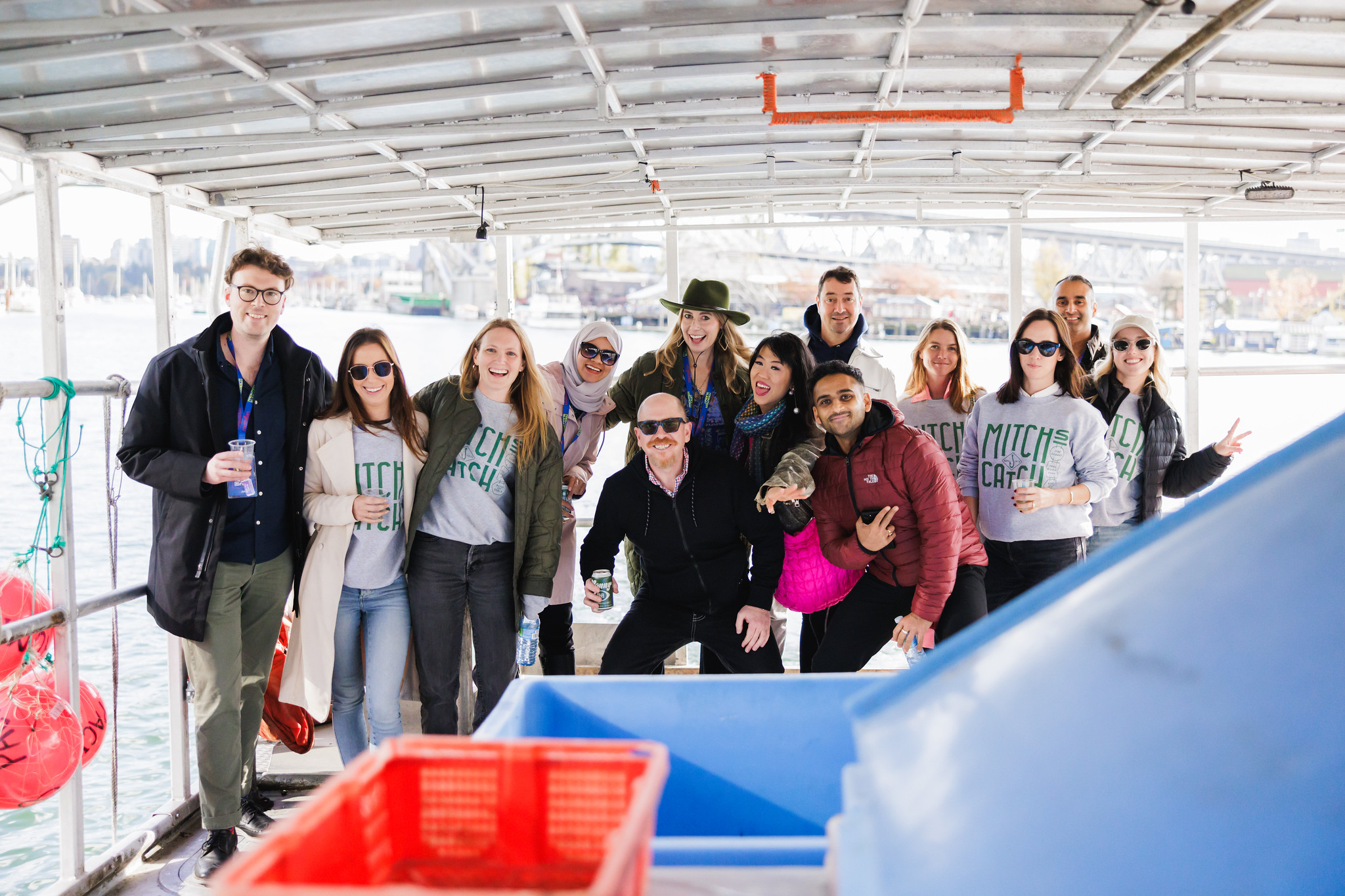A group in matching sweatshirts poses together aboard a covered fishing boat in Vancouver harbour.