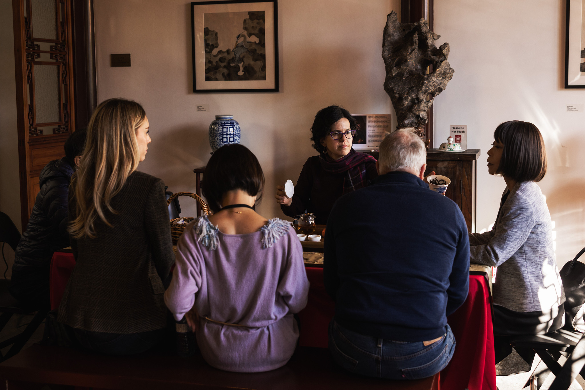 A small group seated around a low table for a tea ceremony in a traditional Chinese garden room.