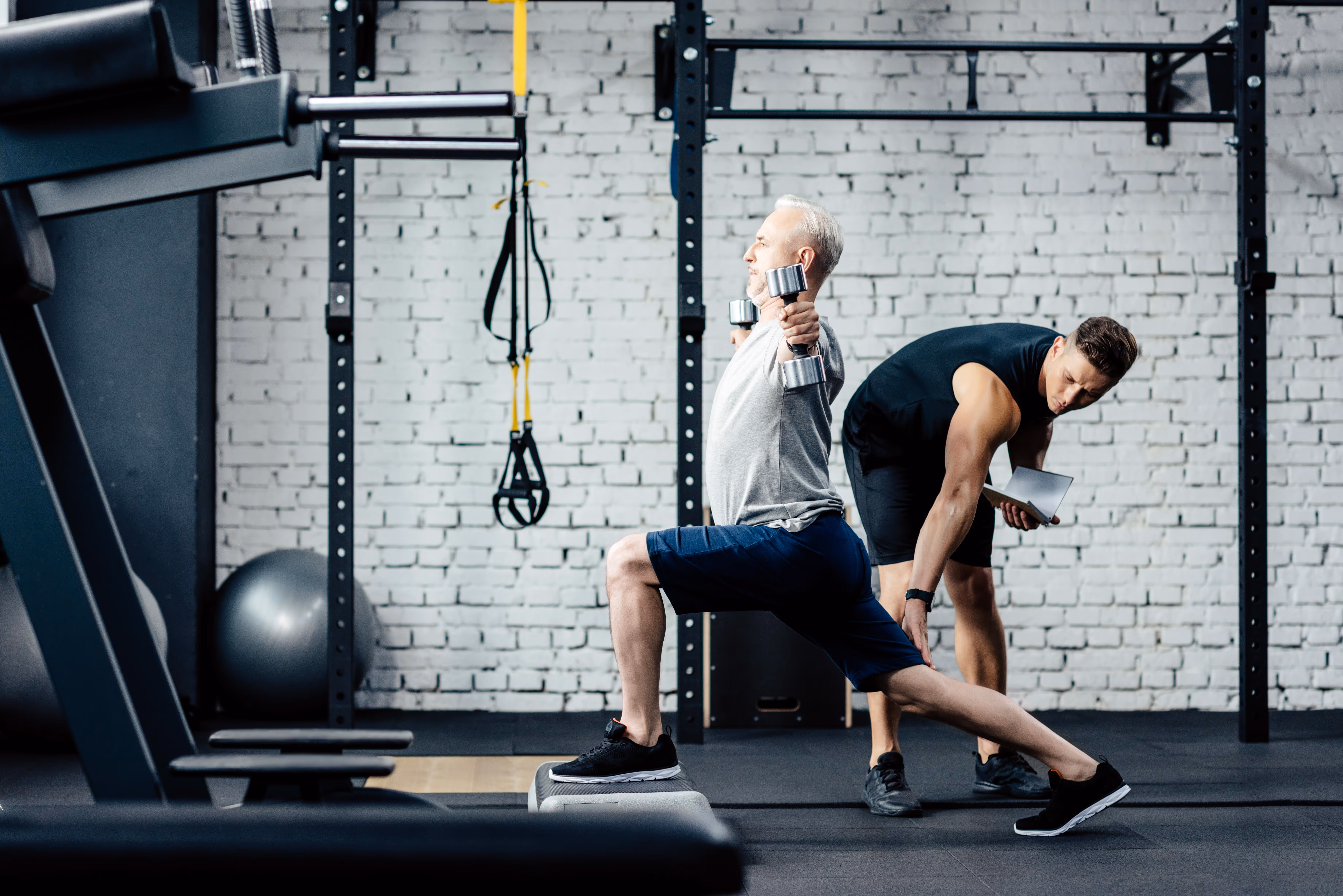A functional personal  trainer demonstrates a primal movement exercise . The trainer showcases proper form for a squat, hinge, or lunge, emphasizing strength, mobility, and functional fitness in a well-equipped studio.