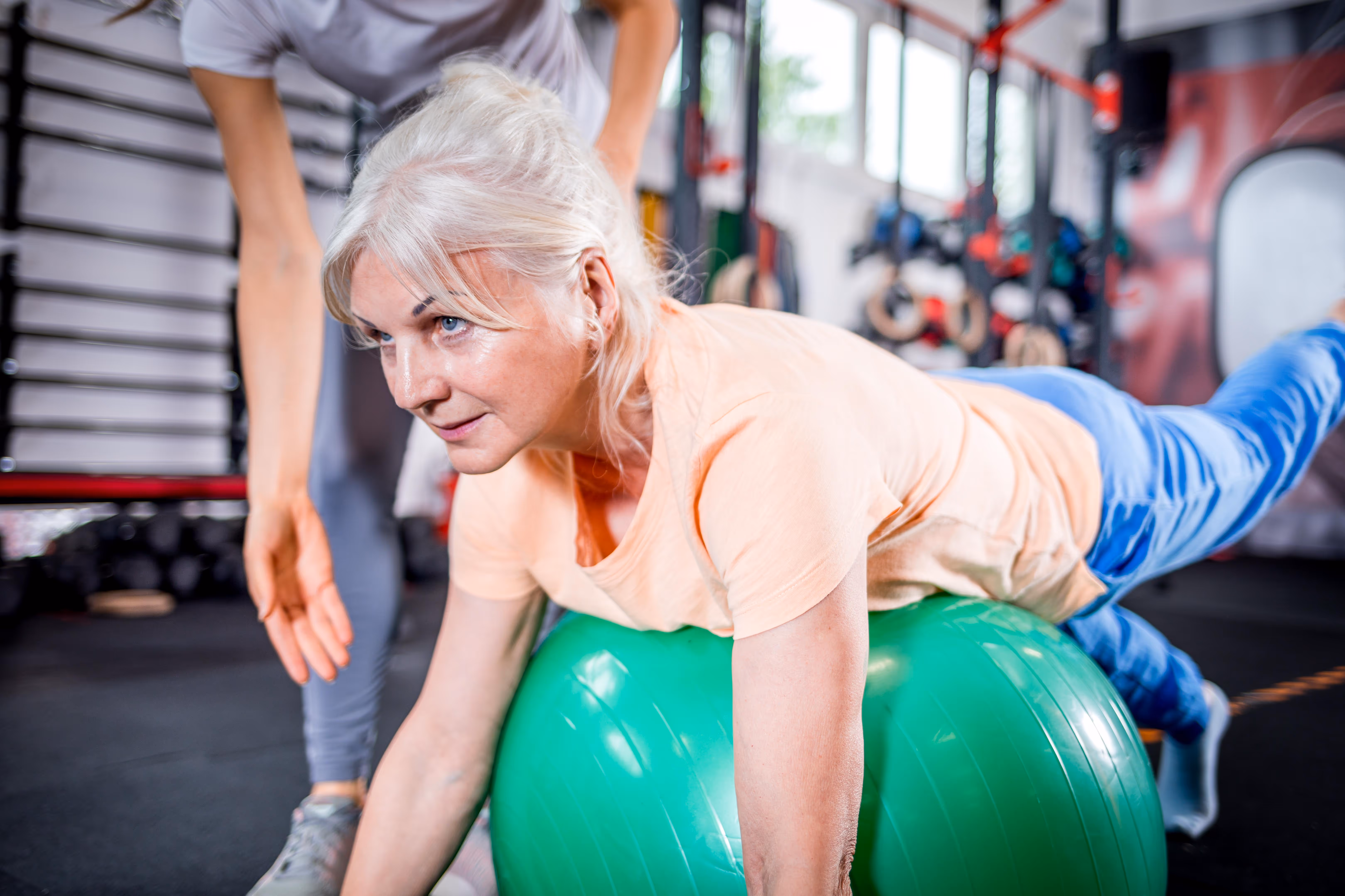 A personal trainer demonstrating a mobility technique. The focus is on improving flexibility, reducing muscle tension, and enhancing overall physical well-being in a calm, supportive studio environment.