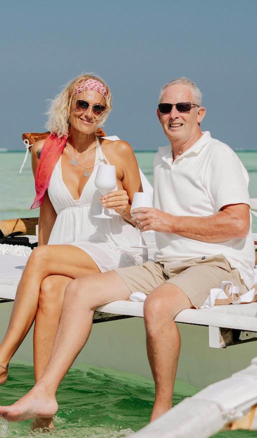 A couple dressed in white sit on retreat dock over the ocean