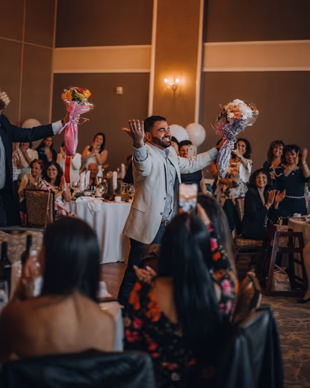 A groom enters a wedding reception at a hotel booked on Pilot holding flowers. 