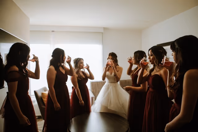 A bride and her bridal party drink a beverage in a Pilot hotel room. 