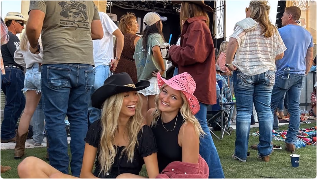 Two women at a concert wearing a black and pink cowboy hat