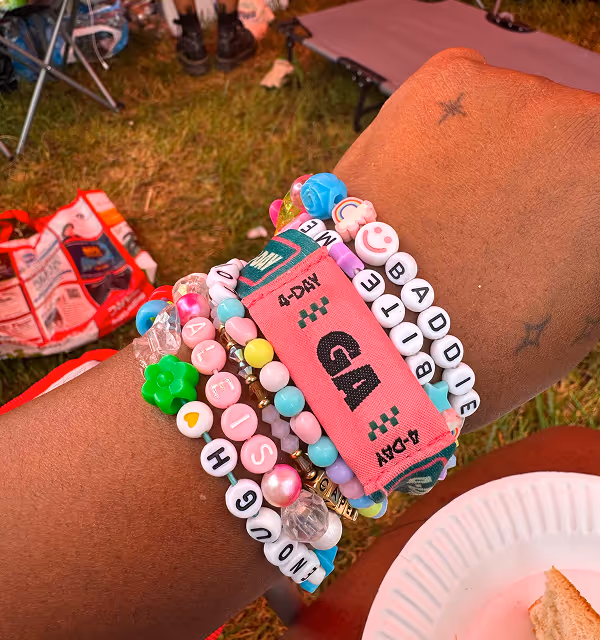 A wrist with a pink general admission bracelet and multiple friendship bracelets