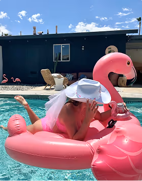 A woman wears a white cowboy hat with vail on a pink flamingo pool raft at a bachelorette weekend planned on Pilot. 