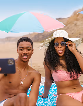 An black couple poses for a playful selfie while sitting on the beach during a romantic beach getaway planned on Pilot. 