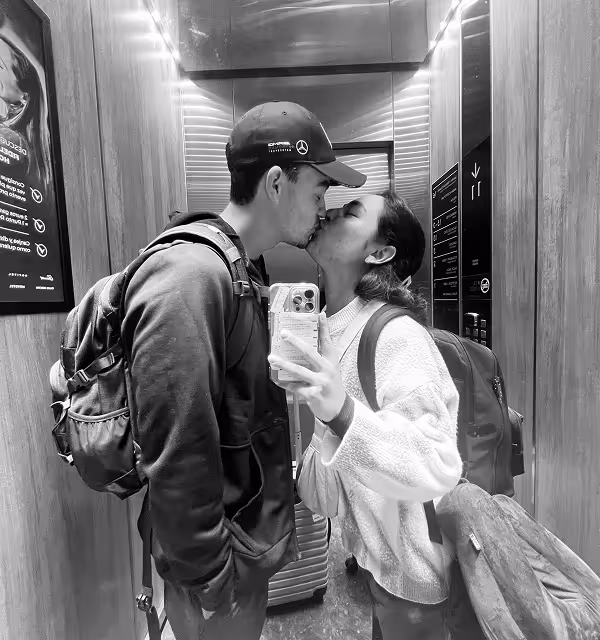 a couple takes a selfie in black and white while kissing in an elevator. 