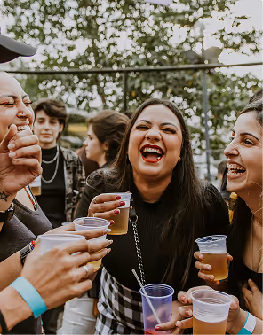 Group of young women laughing and holding plastic cups with beverages at an outdoor gathering, during a backpacking trip planned on Pilot.