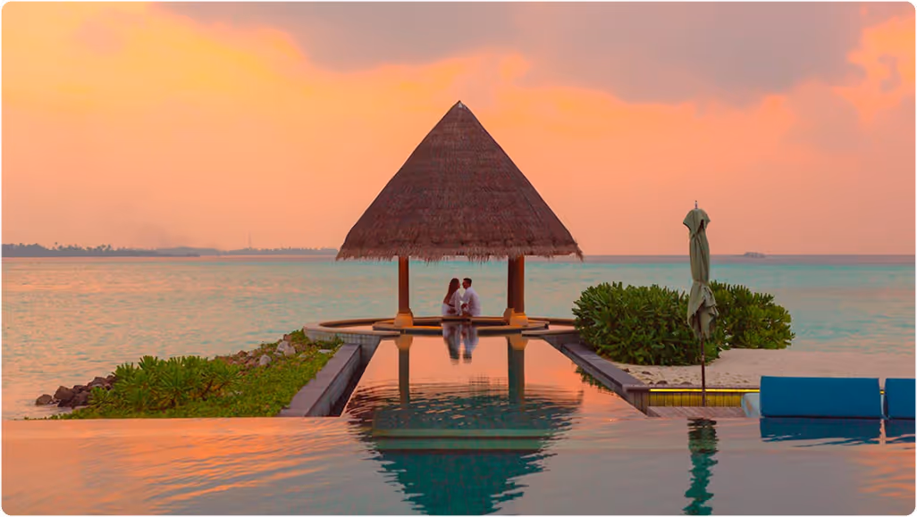 Couple sitting under a thatched gazebo by the ocean during a colorful sunset, during their honeymoon planned on Pilot.