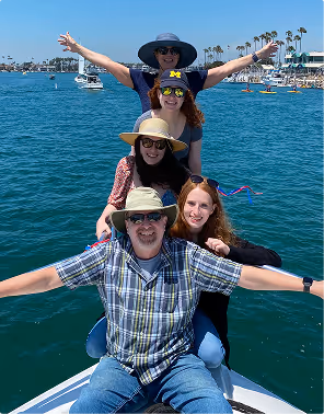 Five people smiling and posing on a boat with blue water and a marina in the background, during a family trip planned on Pilot.