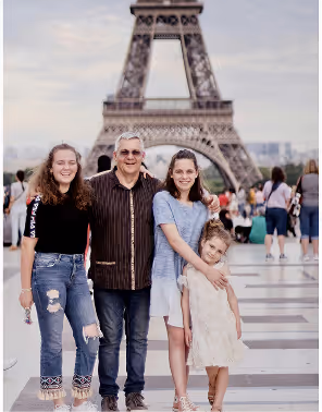 A family of four posing and smiling in front of the Eiffel Tower on a cloudy day, during a family trip planned on Pilot.