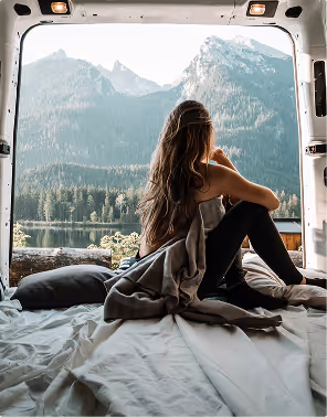 Woman sitting inside a van during a road trip planned on Pilot looking out at a mountain and forest landscape across a lake.