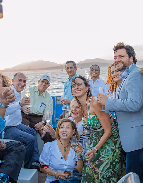 Group of smiling adults while on a trip planned on Pilot enjoying a boat ride with drinks, mountains and sea in the background during sunset.