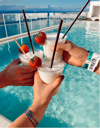 Three people while on a trip planned on Pilot holding creamy cocktails with strawberries and straws by a pool on a sunny day.