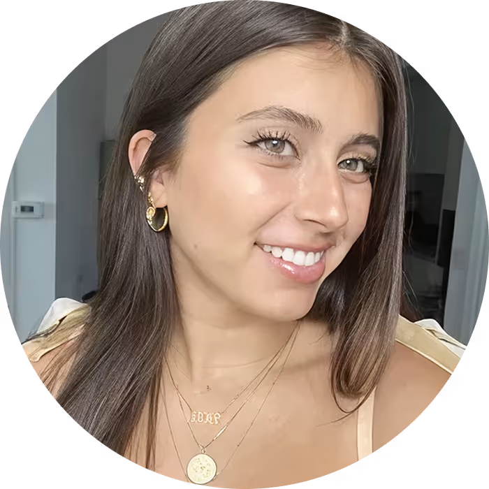 Smiling woman with long brown hair wearing gold hoop earrings and layered gold necklaces.
