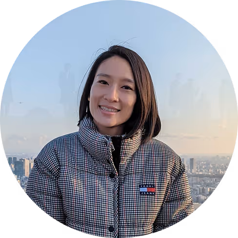 Smiling woman who works for Pilot with straight dark hair wearing a checkered jacket outdoors with cityscape background.