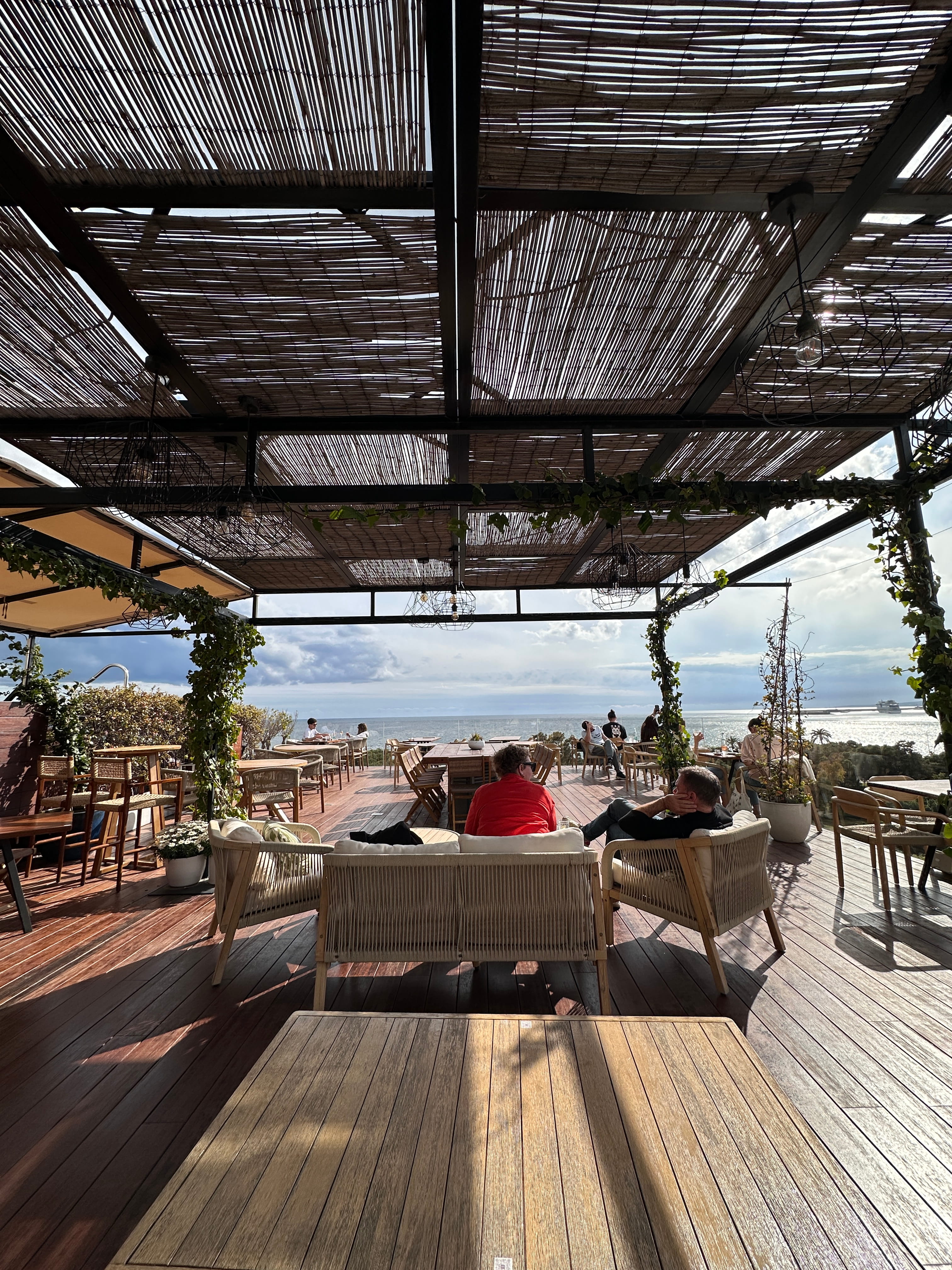 A shaded oceanfront terrace under a slatted pergola roof