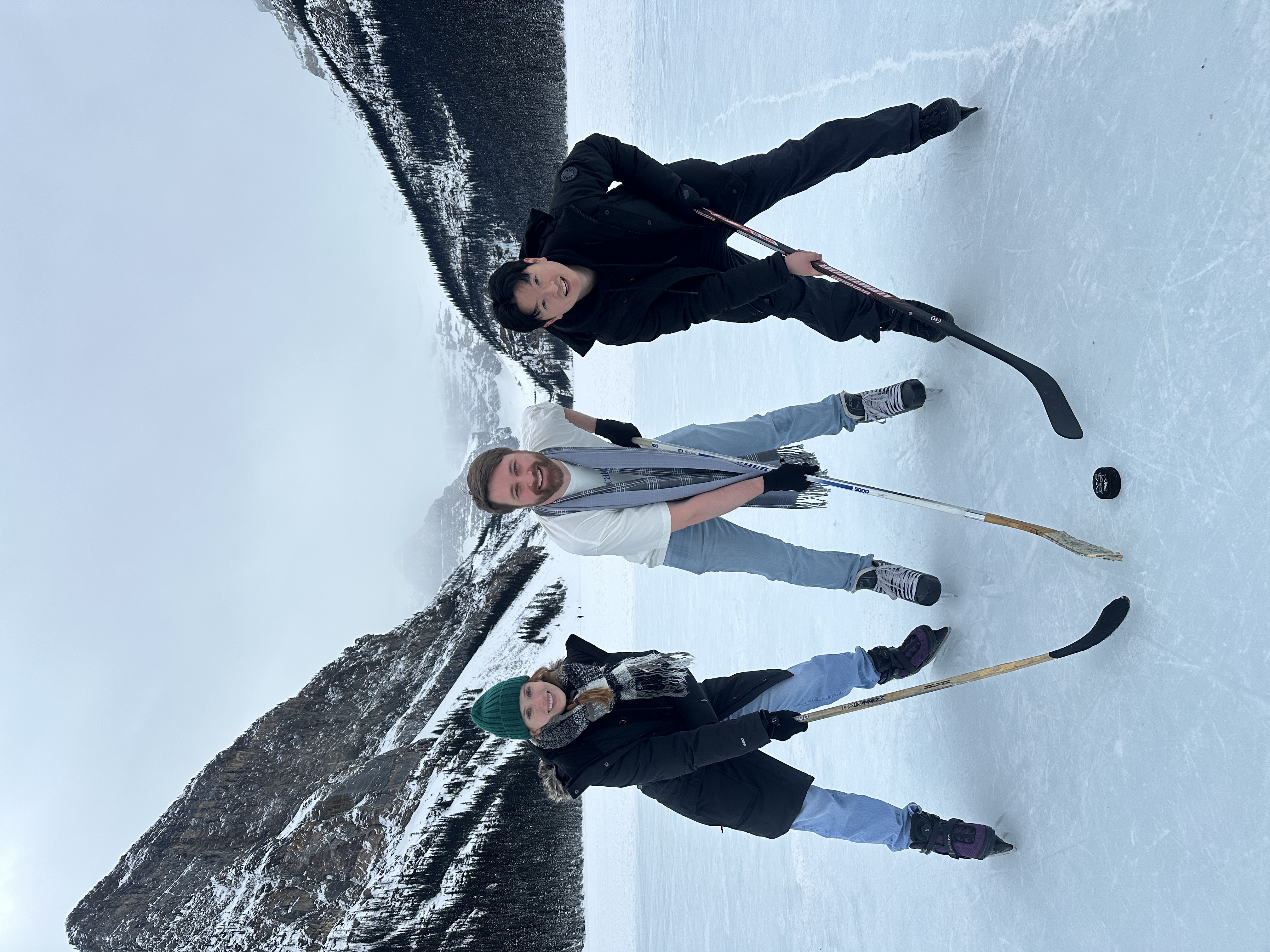 Teammates playing hockey on a frozen lake beneath snowy mountains