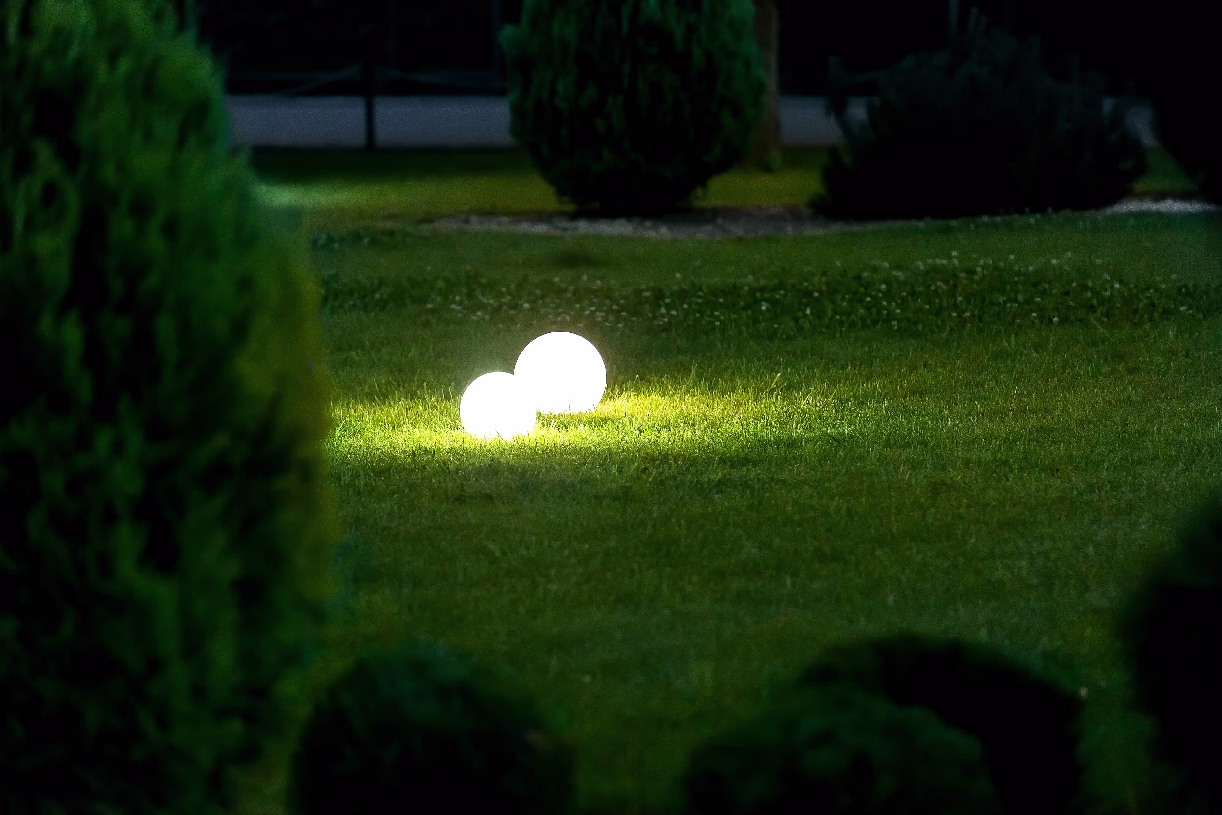 Two glowing white spheres illuminate a dark green garden lawn at night