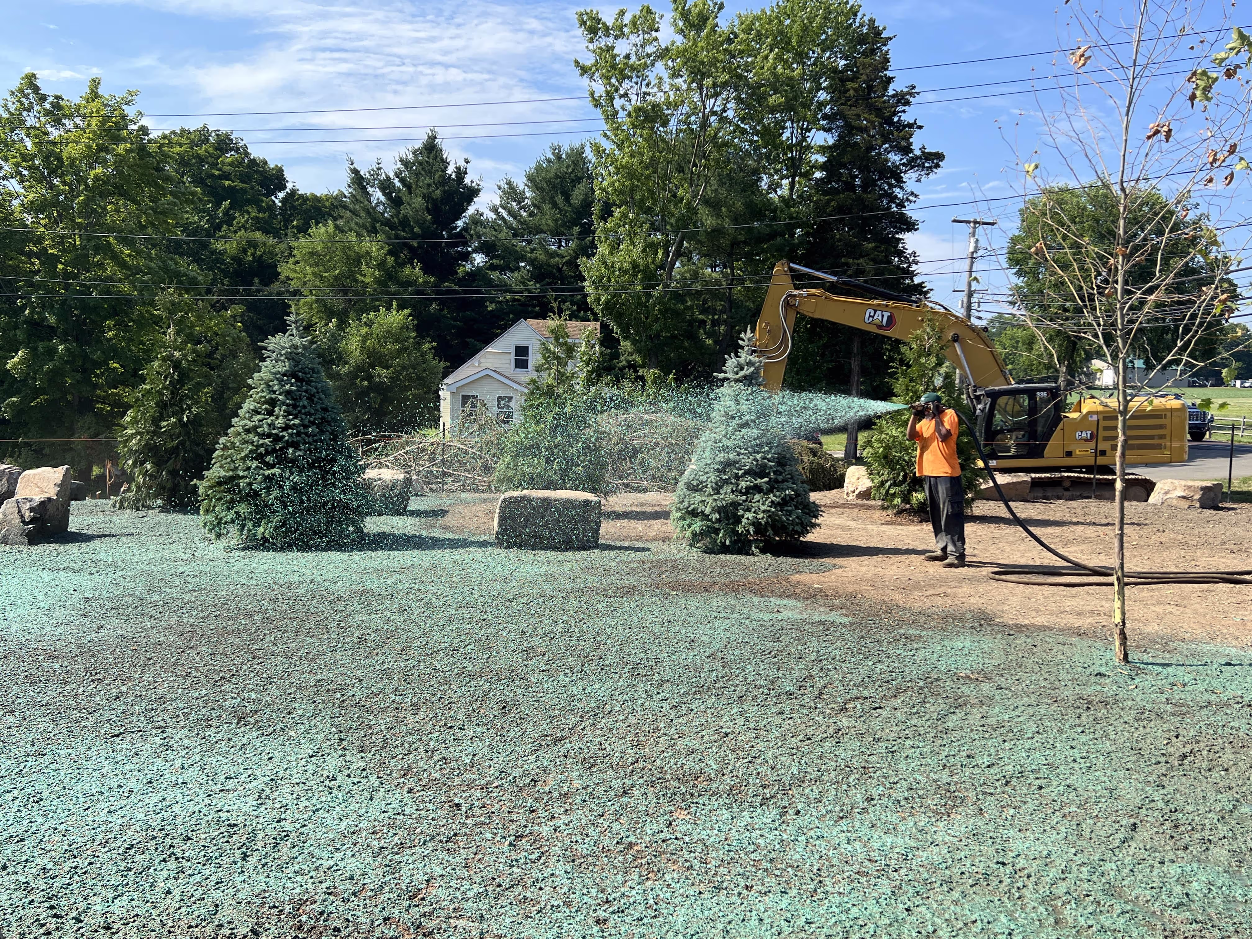 Worker spraying hydroseeding green mulch on landscaping area with excavator