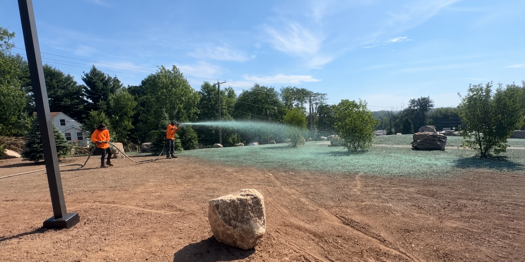 Hydroseeding in progress — green slurry spraying across bare graded ground in Connecticut
