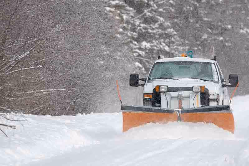 a white truck snow plowing a snow covered street demonstrating snow removal of Vanguard Home Remodeling Group