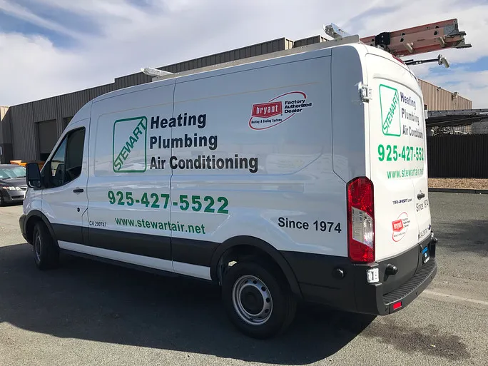 A white commercial service van for 'Stewart Heating Plumbing Air Conditioning,' branded with the company name, phone number, website, and the 'Bryant Factory Authorized Dealer' logo