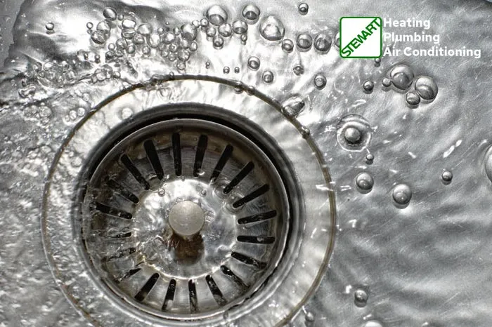 Water flowing into kitchen sink drain with bubbles, featuring STEWART Heating Plumbing Air Conditioning logo