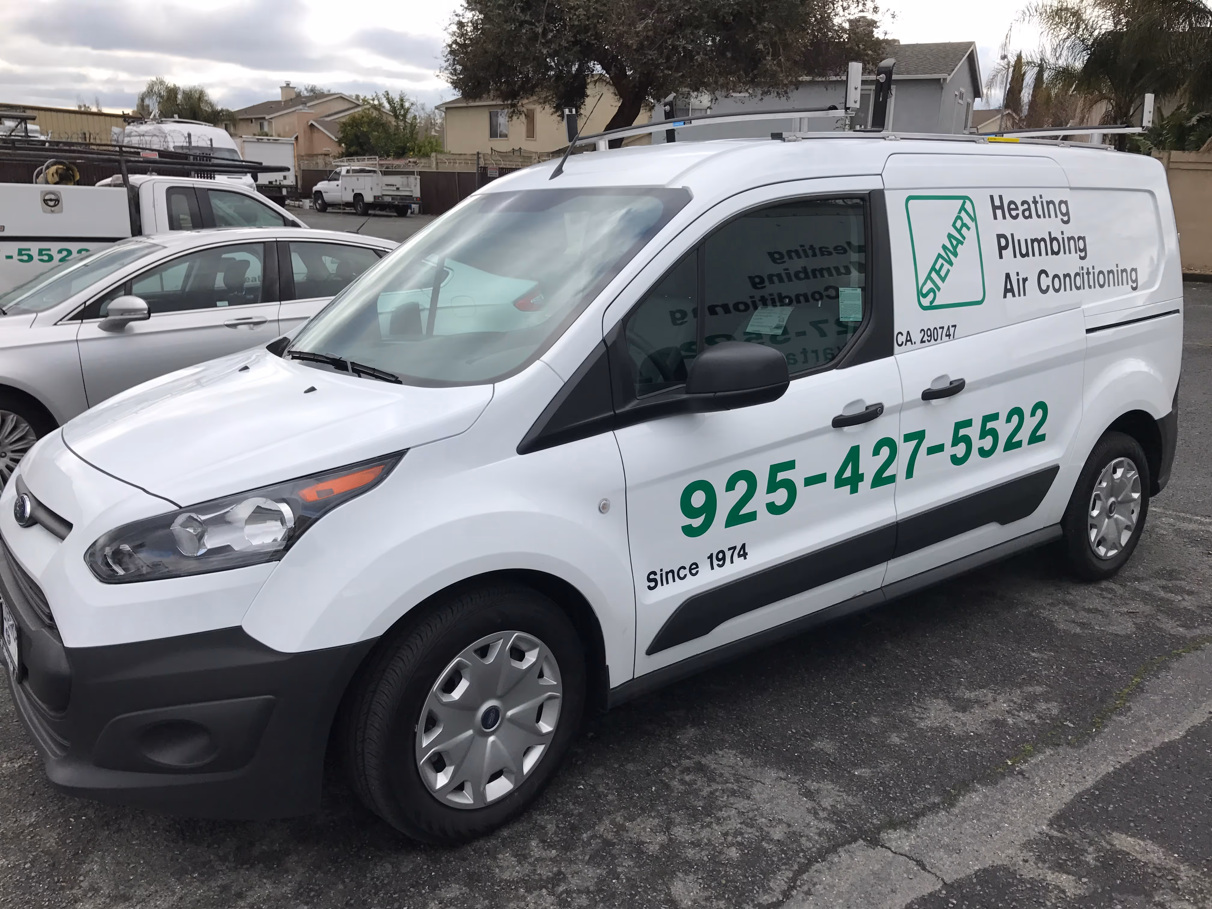 A white commercial van with "STEWART Heating Plumbing Air Conditioning" written in green on its side, along with a phone number "925-427-5522" and "Since 1974," is parked on an asphalt lot.