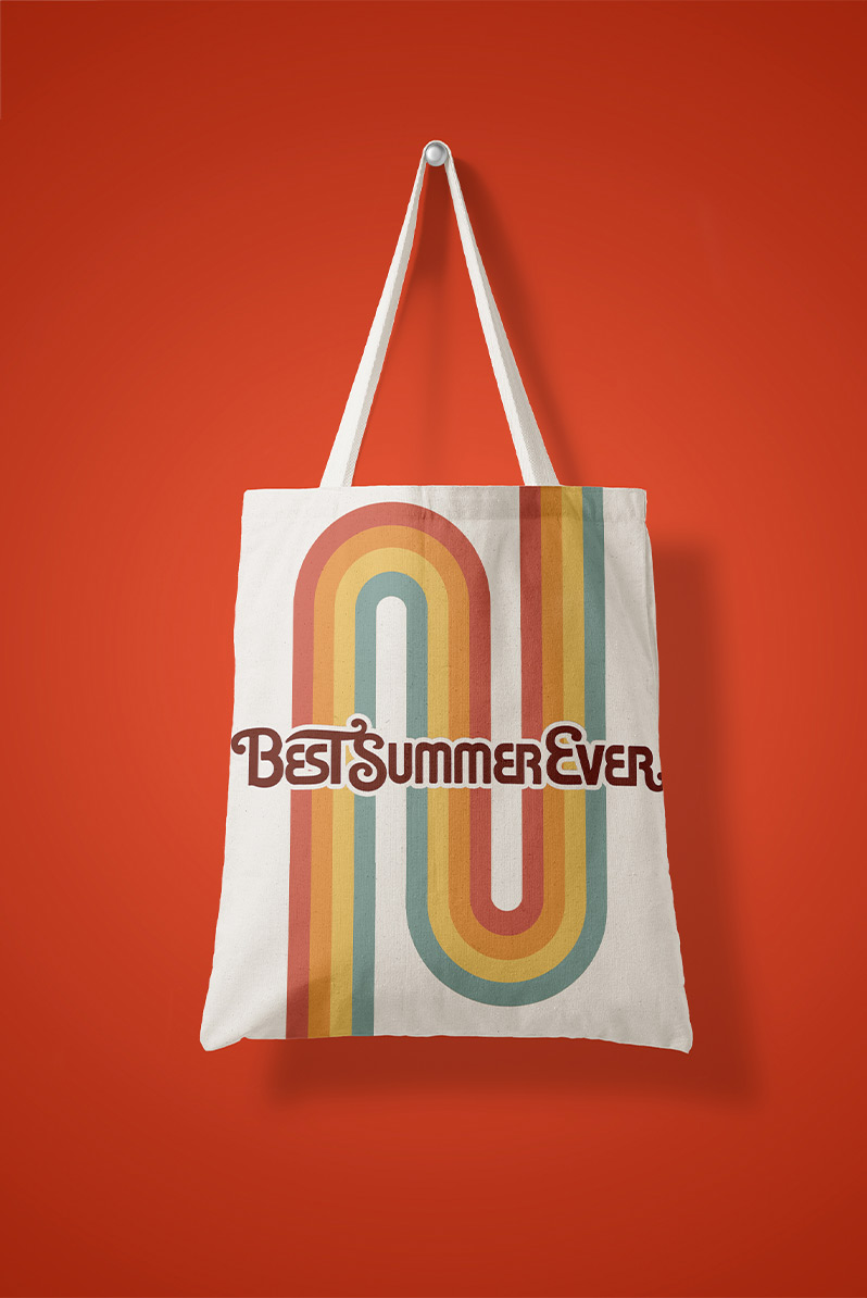 This is an image of a cream-colored tote bag on a red backdrop. The tote is emblazoned with the film's logo, and features a rainbow on a geometric path. The tote has a 70s vibe.