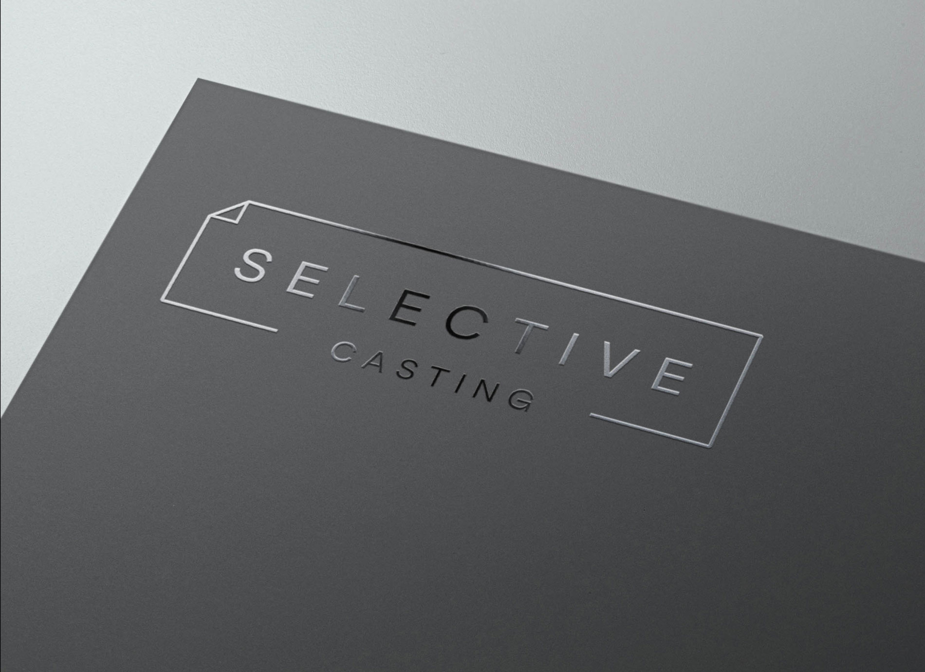 This is an image of a binder for Selective Casting. The background is light grey and the binder is dark grey with the logo embossed in the top left corner in a glossy black application.