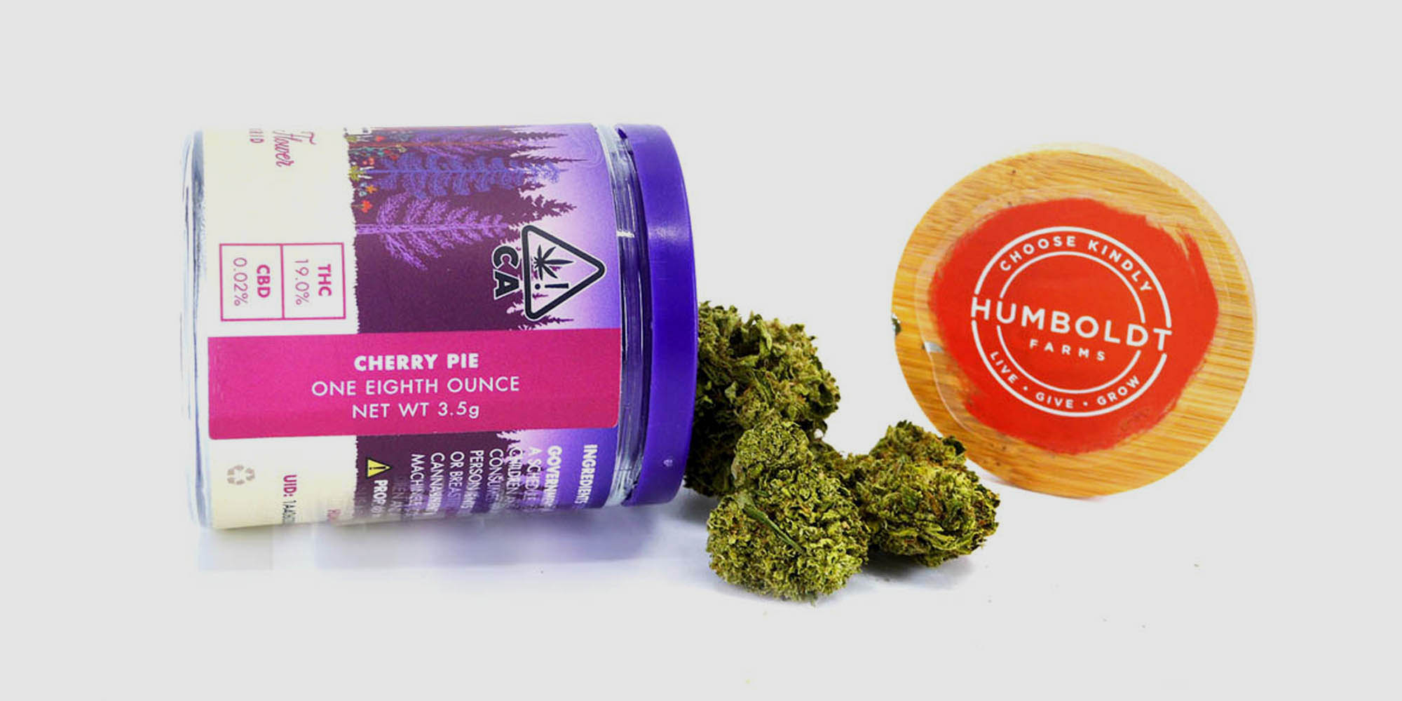 This is an image of a purple container containing loose marijuana flower from Humboldt Farms, laying on its side with flower spilling out of it. This particular container/jar has an eighth ounce of a hybrid marijuana called Cherry Pie.
