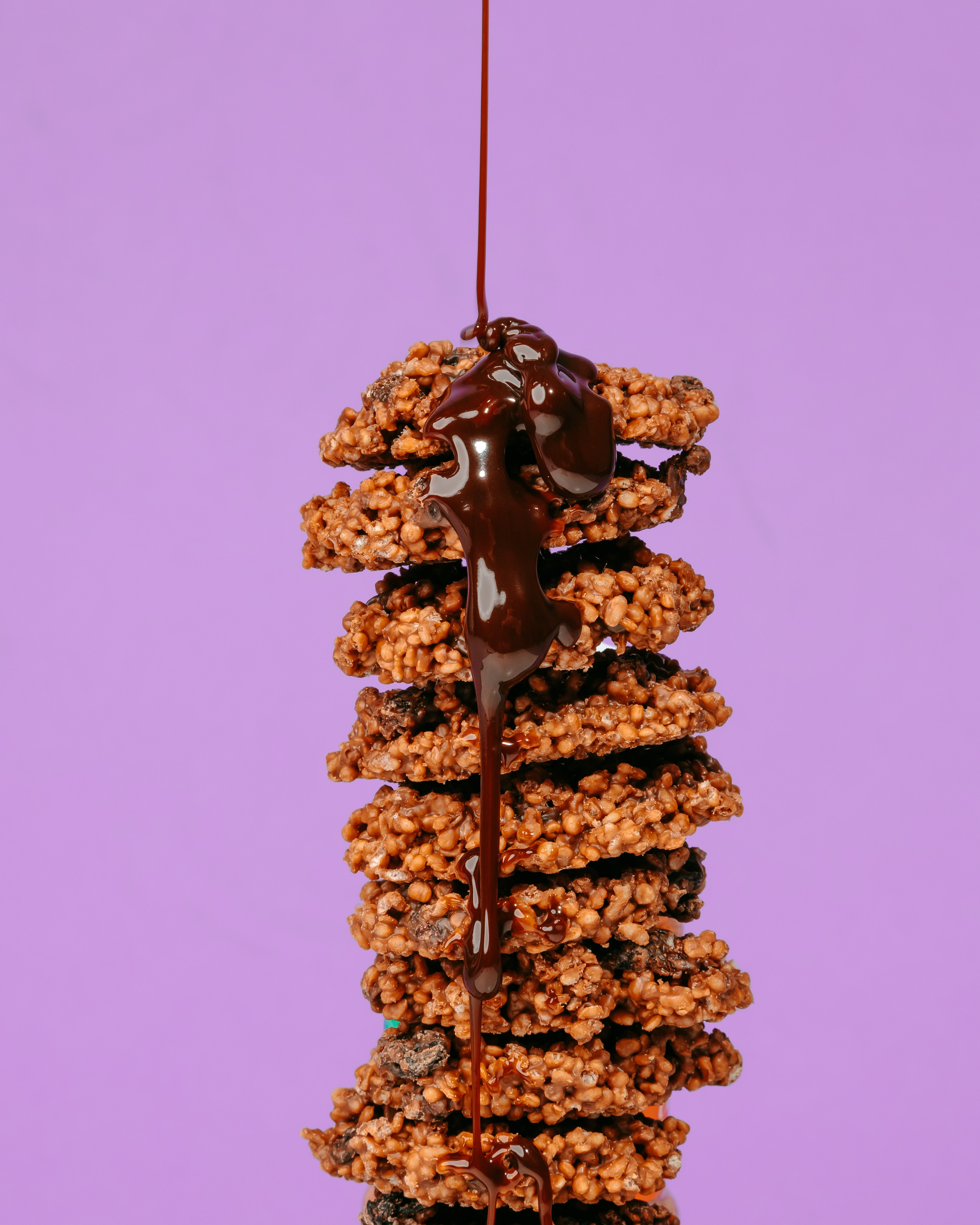 This is an image of a stack of Florentine cookies with chocolate being drizzled over them, set against a lavender background.