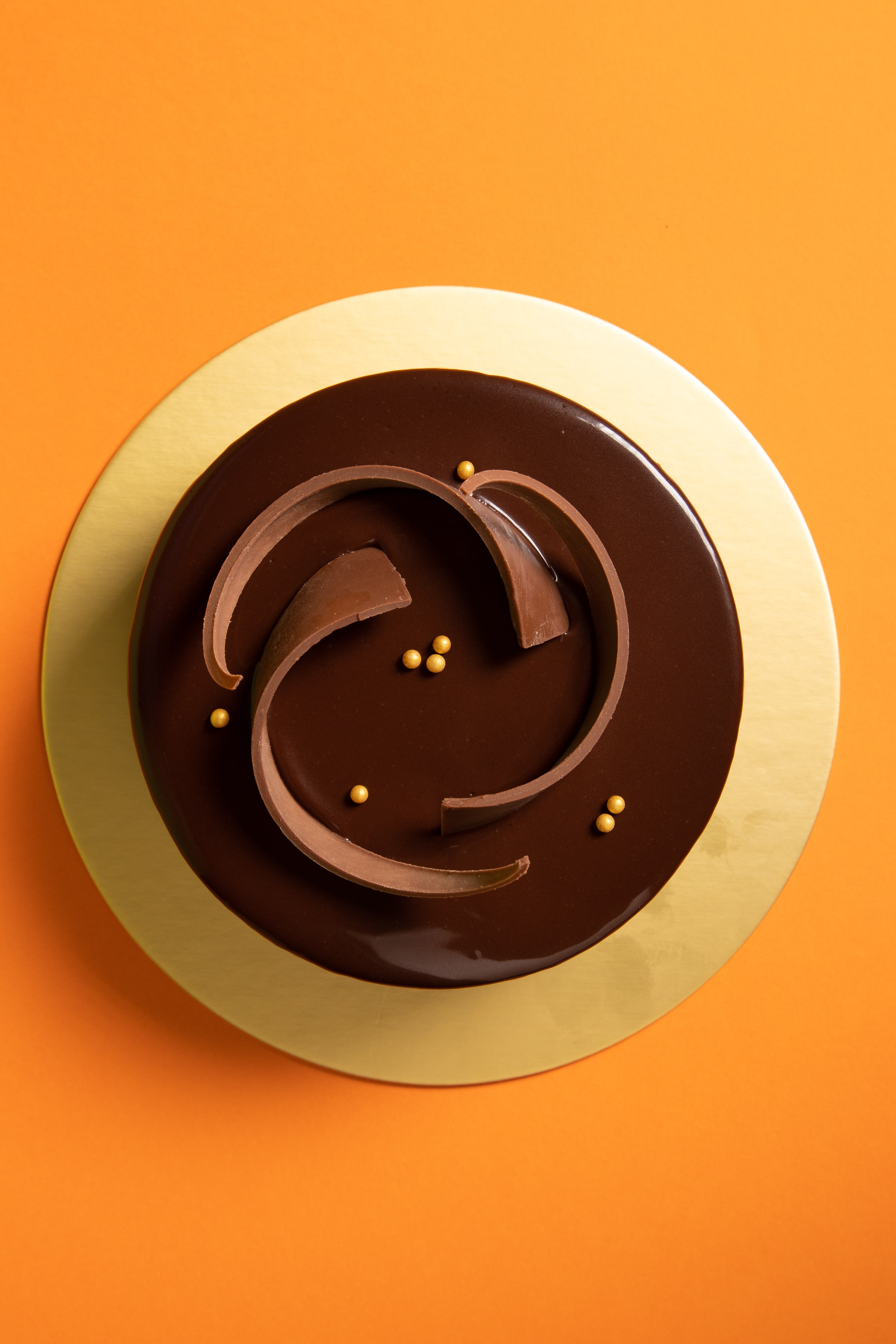 This is a photograph of a cupcake (or a cookie?) with only the top visible. There's a yellow cake/cookie and chocolate frosting with a few sprinkles set on a saffron yellow background.