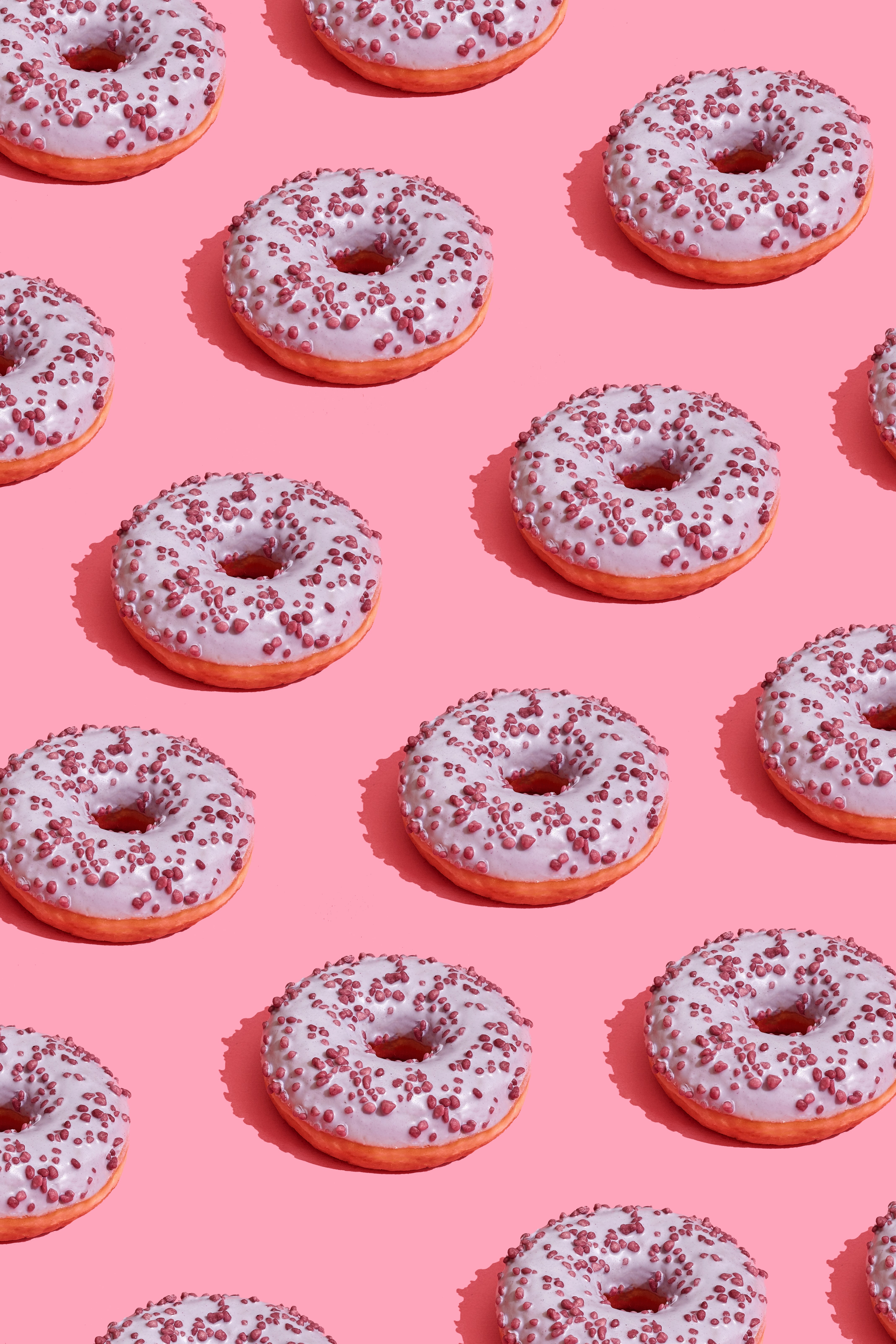 This is an image of pink frosted donuts, on a grid, on top of a pink background. It's the kind of image that can be shared on social media because of its aesthetic.