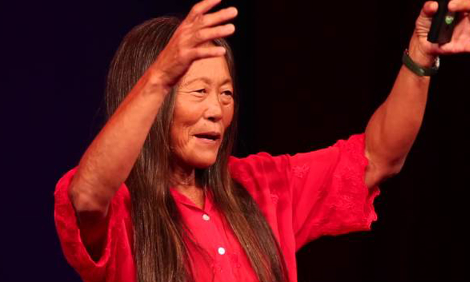 Image of Peggy Oki wearing a bright red shirt, arms raised.