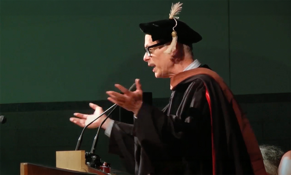 Picture of John Waters giving a speech in a black doctoral hood