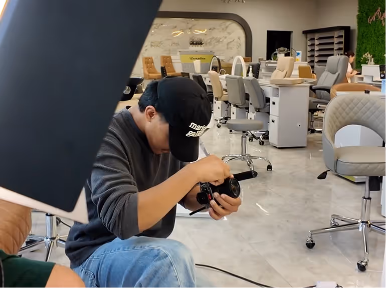Person wearing a black cap adjusting a camera in a modern office with chairs and desks in the background.
