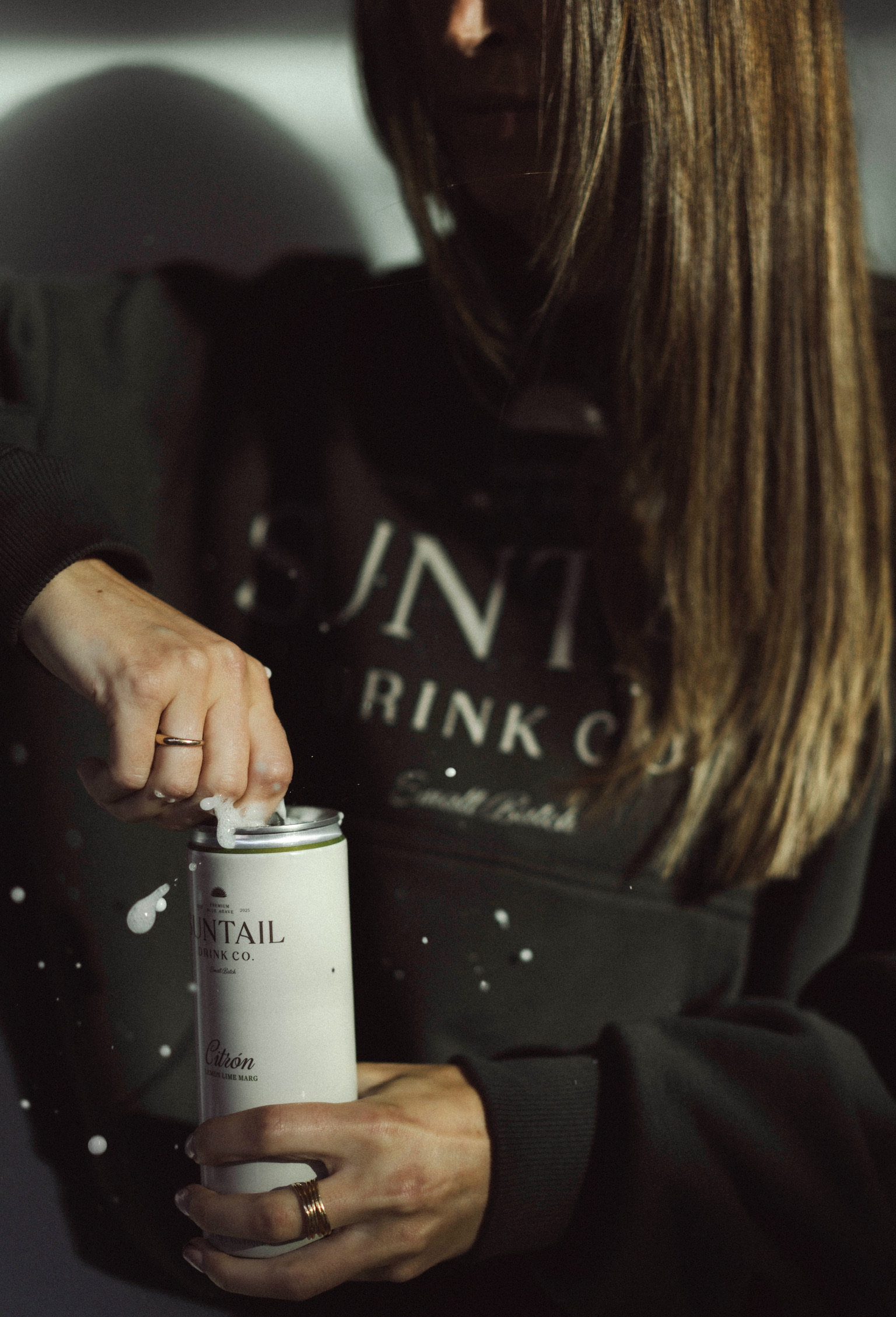 Close-up of a hand holding two Suntail Drink Co. cans, one labeled Citron Lemon Lime Marg, against a black jacket background.