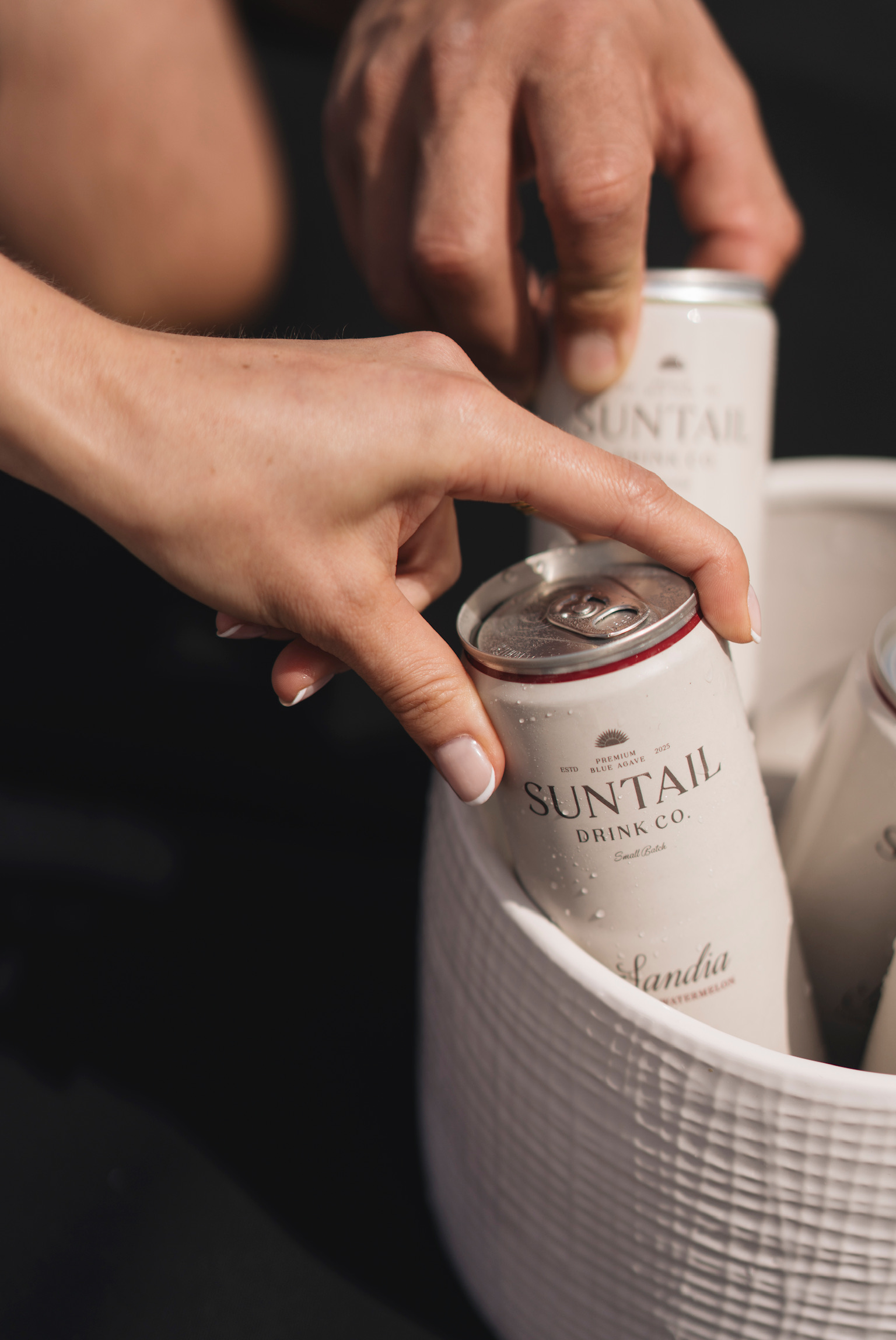 Hand holding a transparent Suntail drink bag filled with lemons and limes next to a red car door.