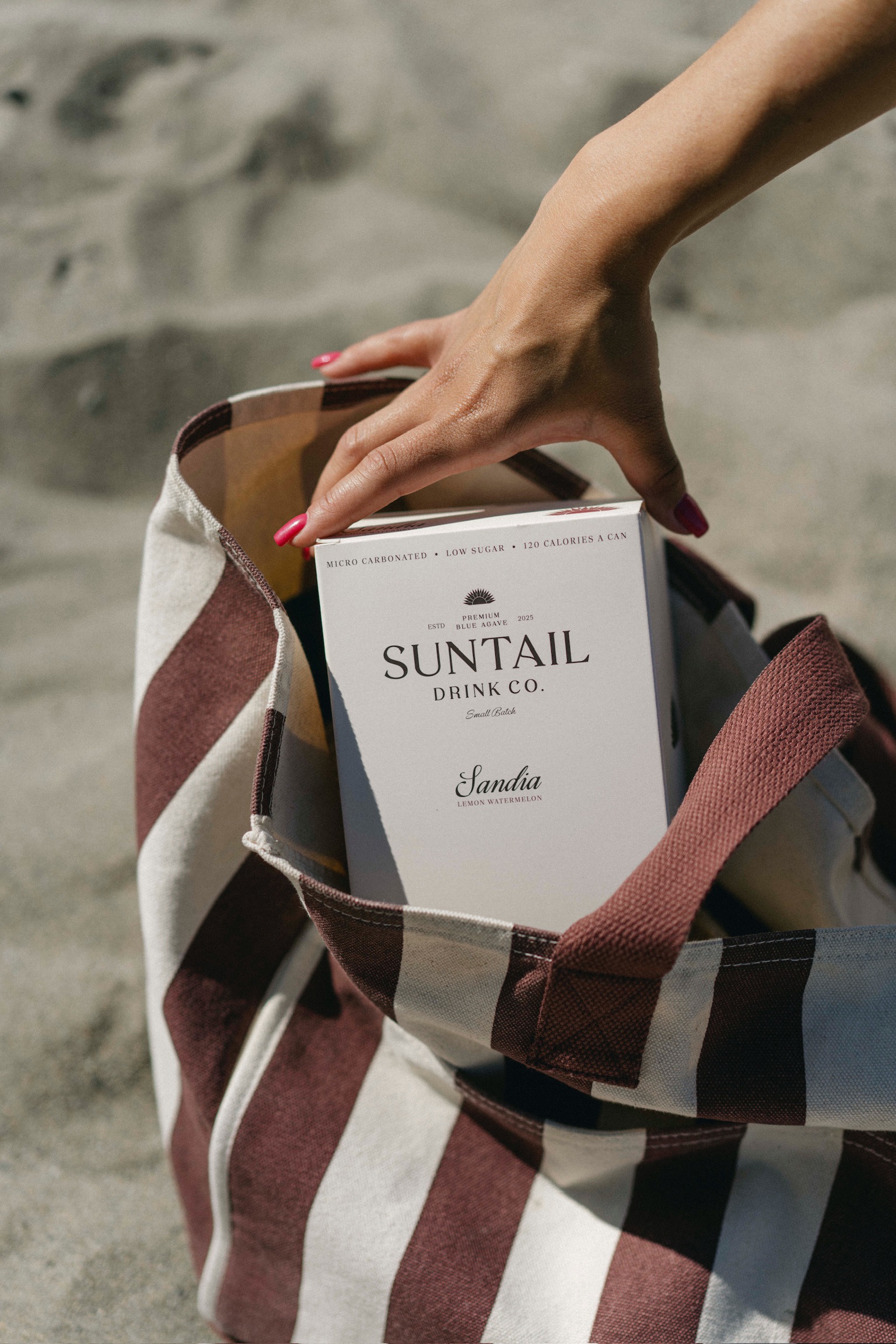 Hand holding metal ice tongs gripping a large round ice sphere against a brown background.